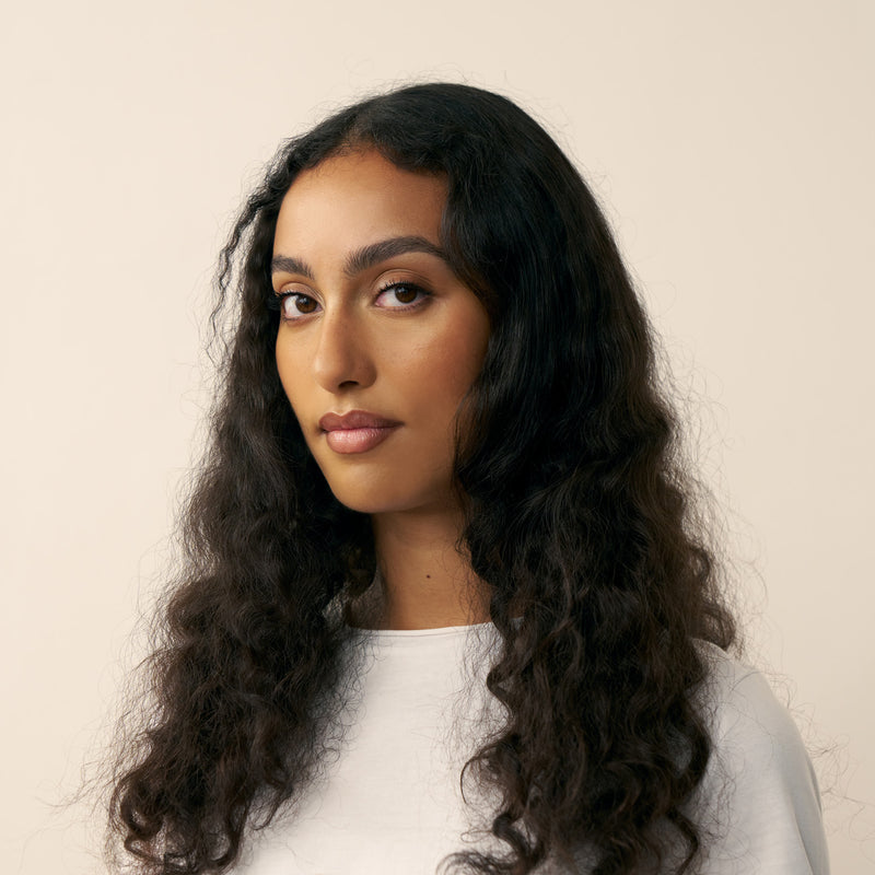Before using the cream. Woman with long, wavy hair wearing a white top against a beige background