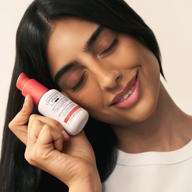 Woman  holding Christophe Robin Regenerating serum close to her face with a neutral background