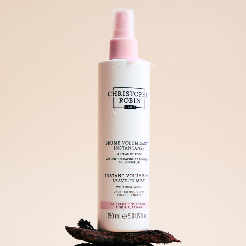 Bottle of Christophe Robin Instant Volumizing Leave-In Mist on a beige background with ingredients 