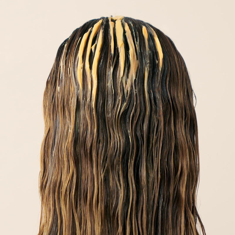 Blonde woman with Christophe Robin Shade Variation mask in golden blonde applied to her damp hair on a beige background