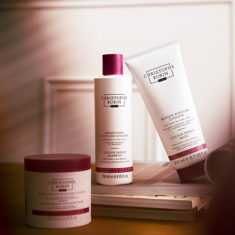 Three Christophe Robin colour shield  products on a wooden surface with a blurred background