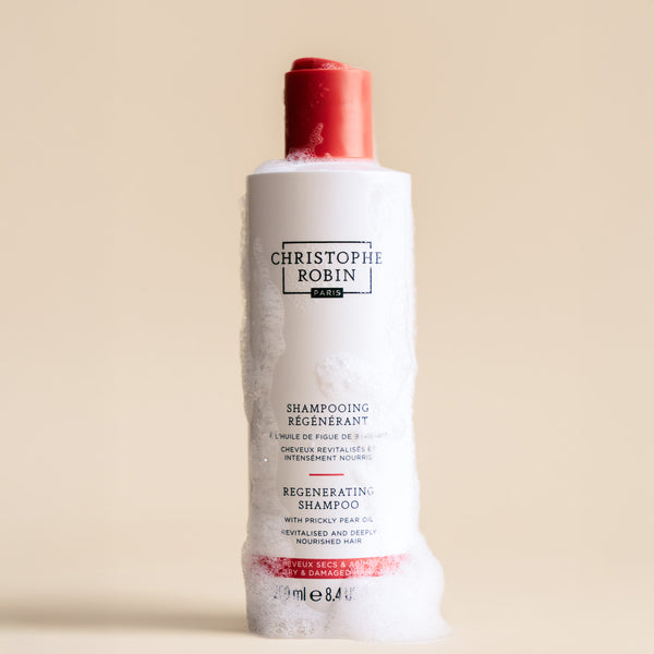 Bottle of Christophe Robin regenerating shampoo 250ml showing foam texture on a beige background