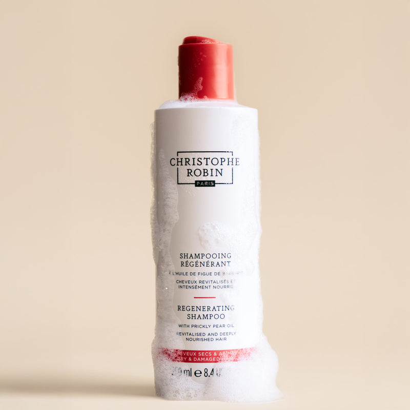 Bottle of Christophe Robin regenerating shampoo 250ml showing foam texture on a beige background