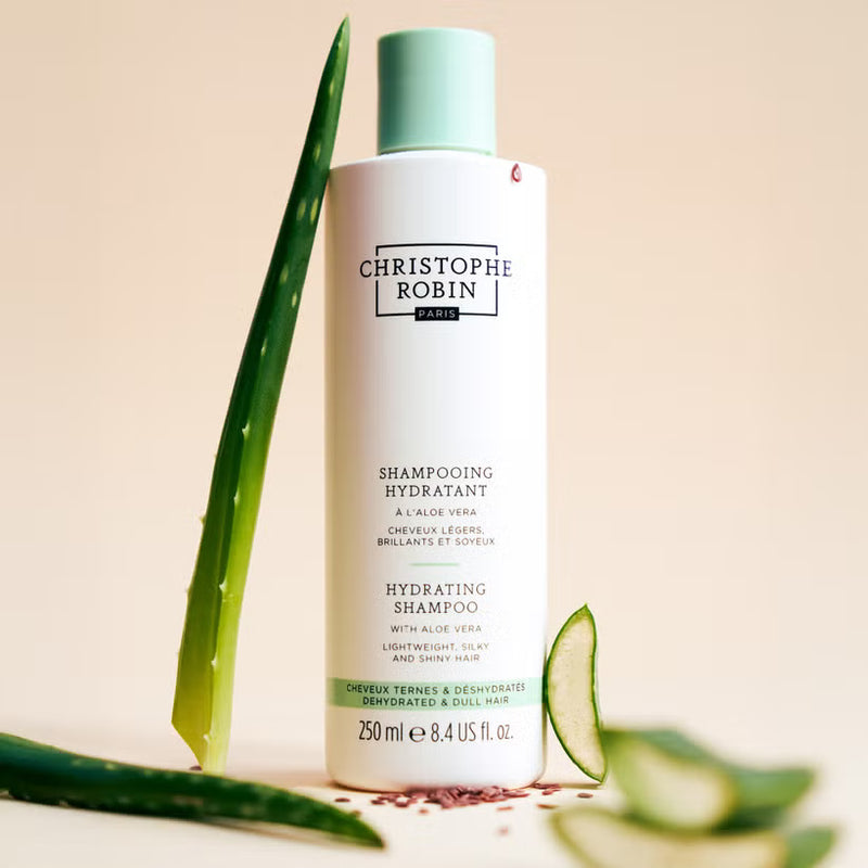 Christophe Robin hydrating shampoo bottle with aloe vera leaves on a beige background