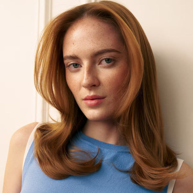 Woman with long brown voluminous hair wearing a blue top against a neutral background